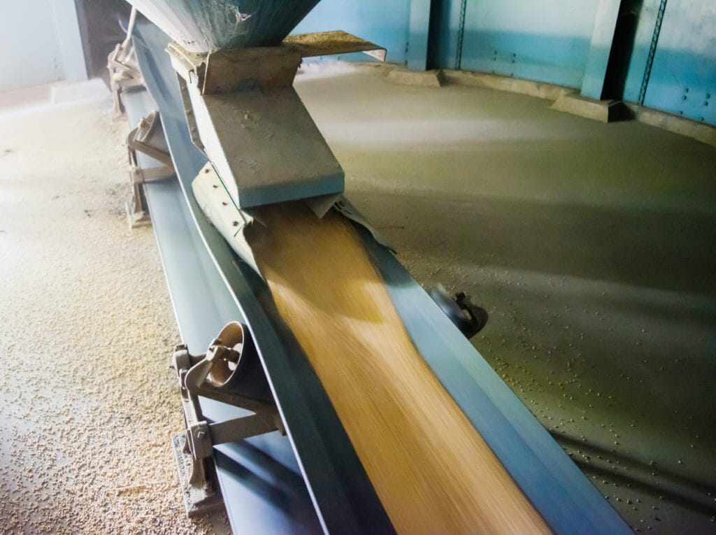 Blue conveyor chute feeding flowing grain into a hopper, industrial bulk handling at a Hi‑Vac facility