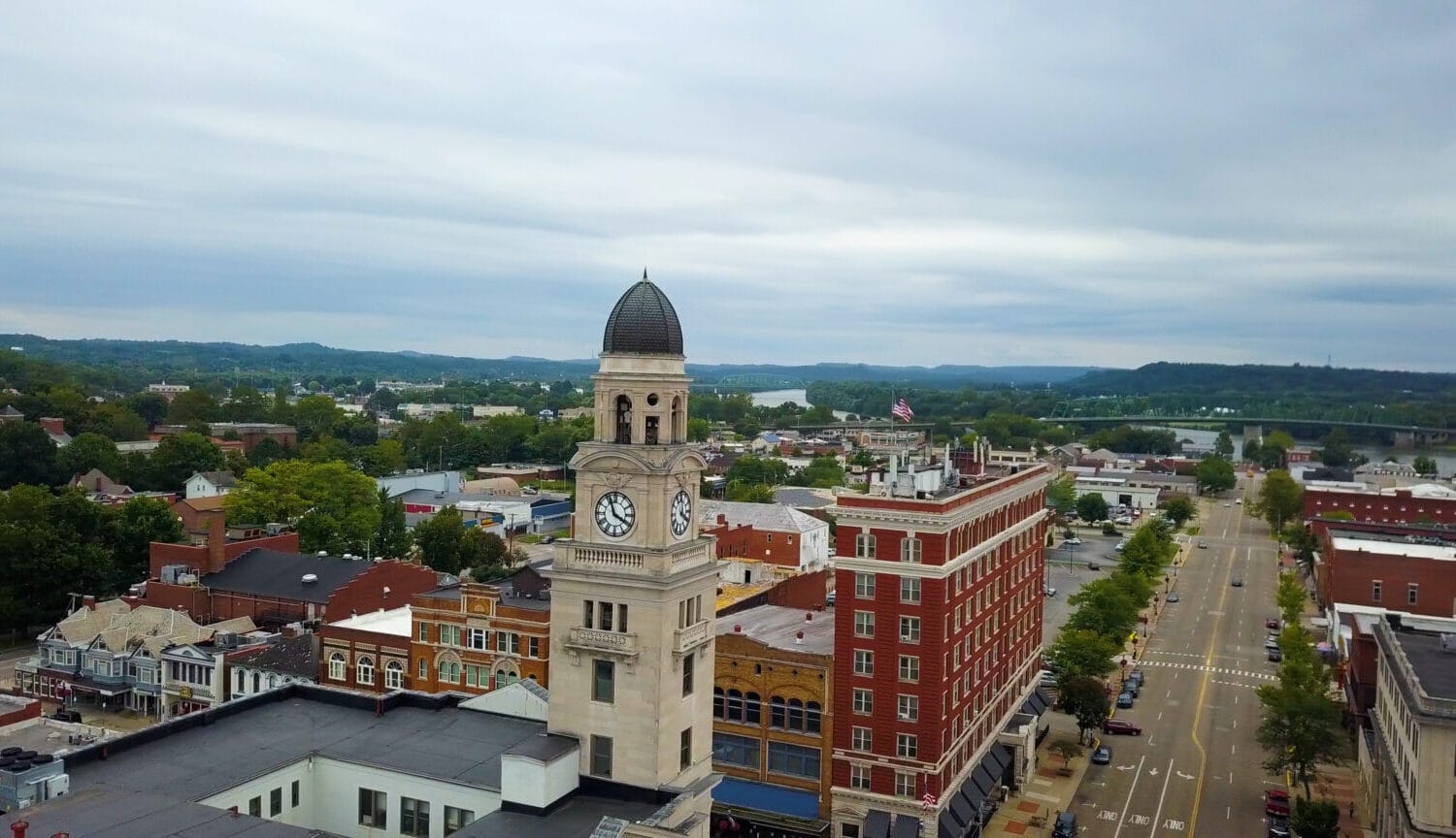 Historic clock tower over downtown streets with river and bridge in the distance, small American manufacturing town.