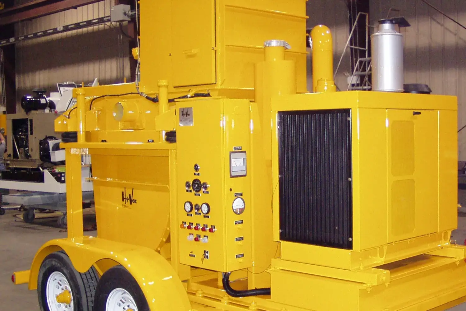 Bright yellow Hi‑Vac industrial vacuum trailer with dual axles, control panel, radiator and exhaust, inside fabrication shop