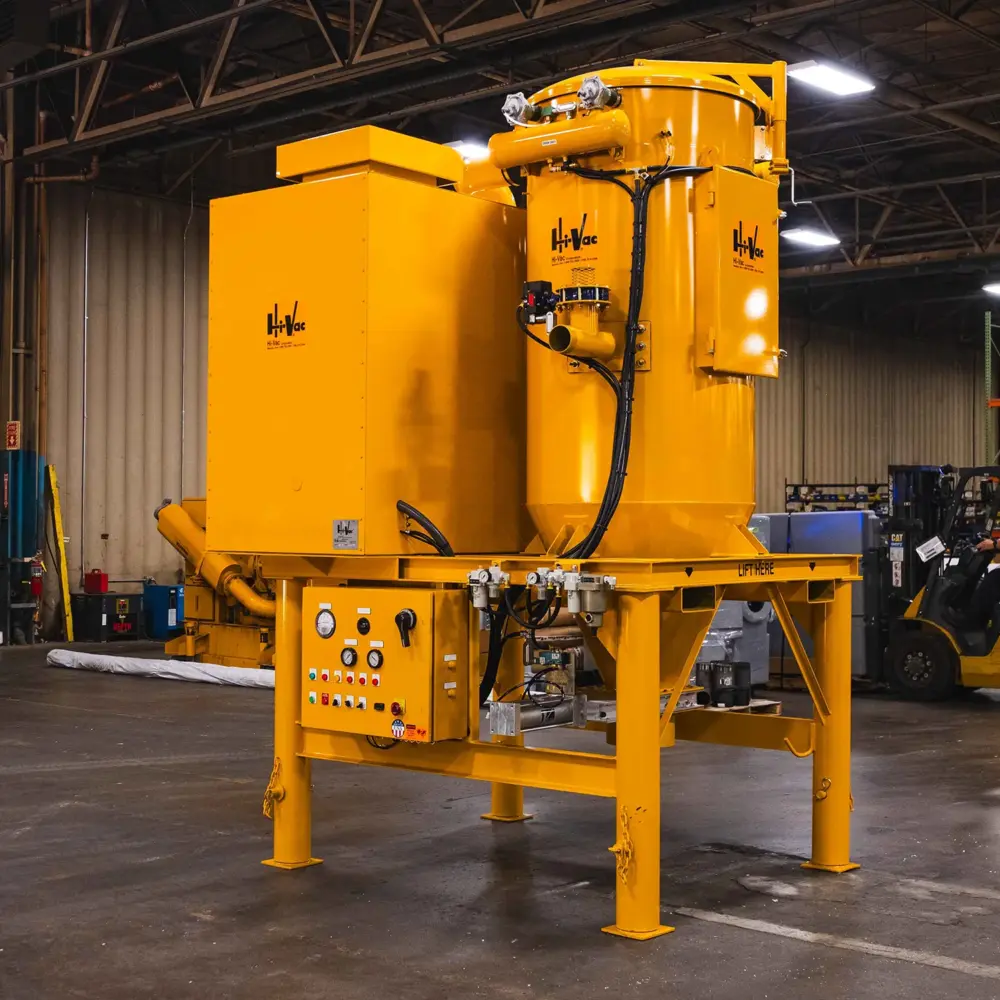 Large yellow Hi-Vac industrial vacuum system with control panel on raised steel frame inside manufacturing warehouse.