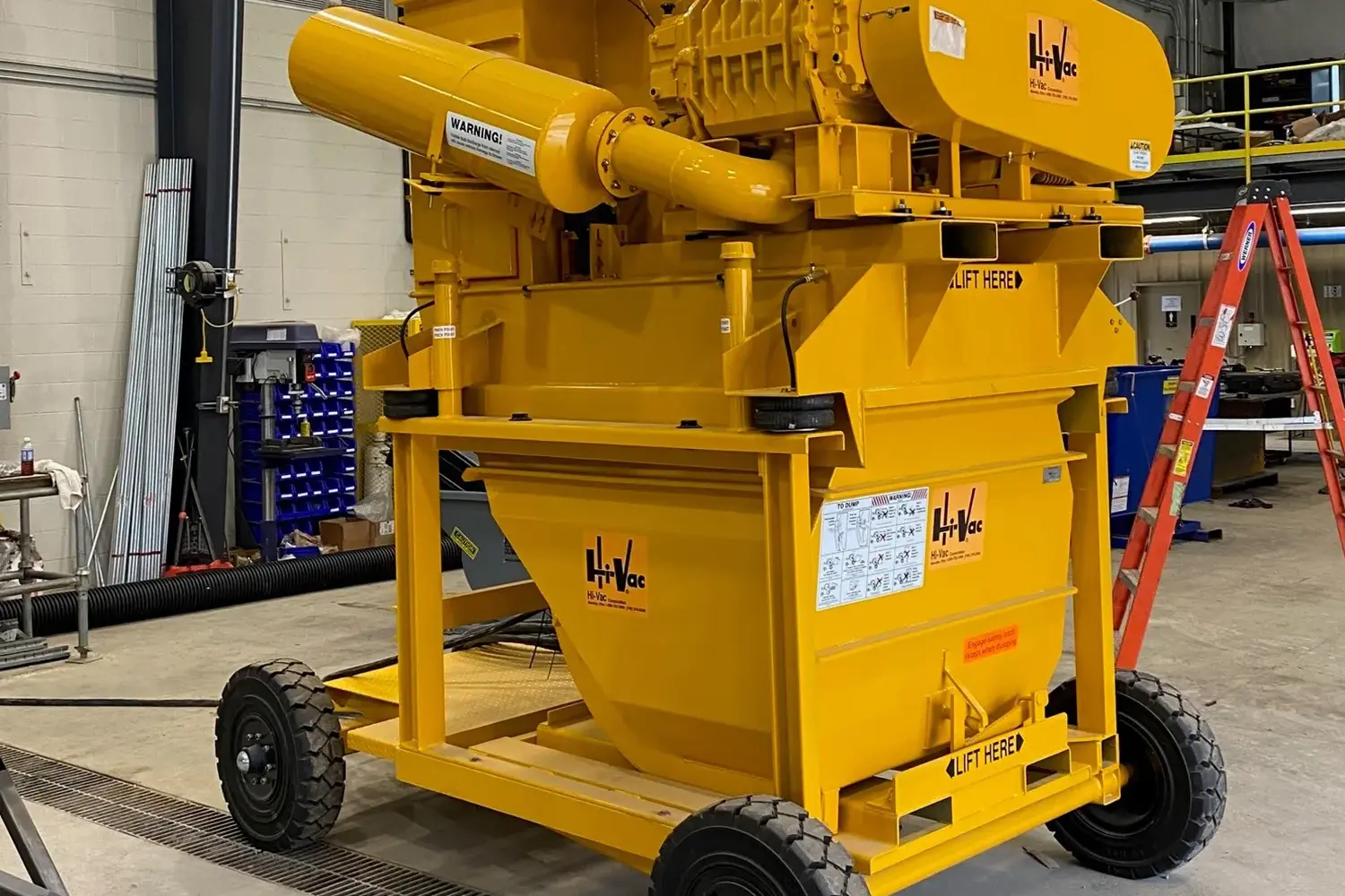 Yellow Hi-Vac portable industrial vacuum hopper and blower assembly on wheeled chassis inside a manufacturing shop.