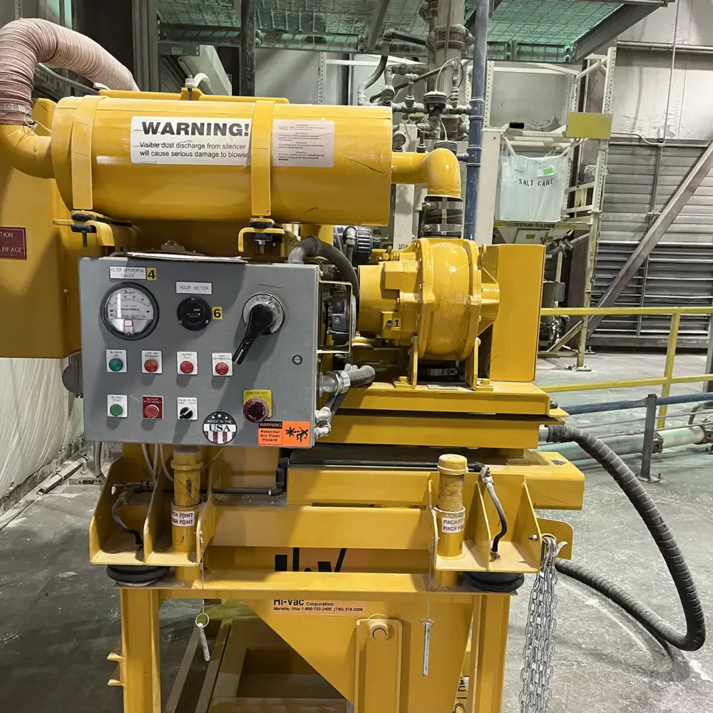 Yellow Hi-Vac industrial vacuum/blower with control panel, gauges and warning label on skid-mounted frame in factory.
