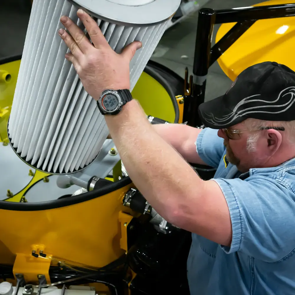 Technician installing large pleated cartridge filter into yellow Hi‑Vac industrial vacuum unit