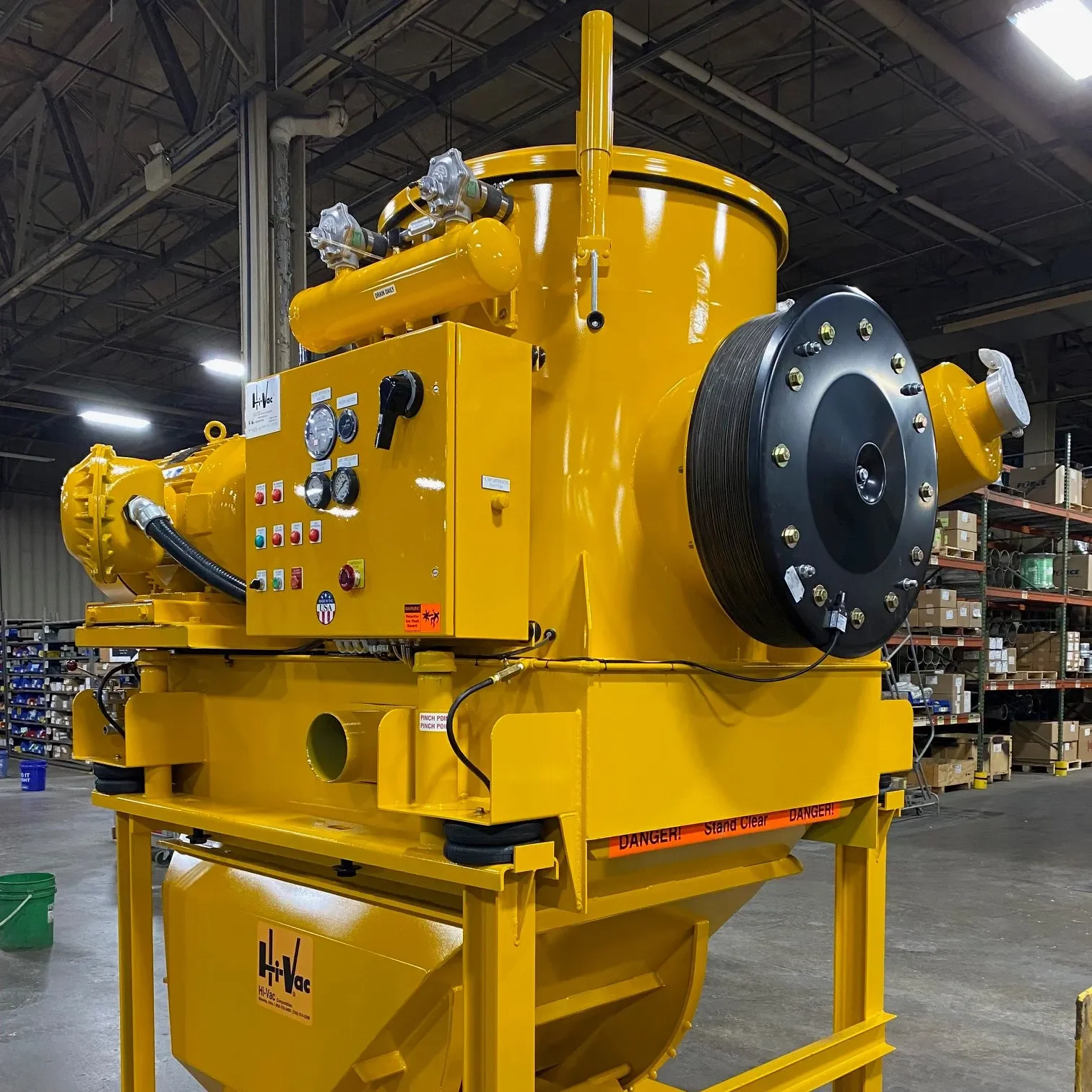 Bright yellow industrial vacuum unit with gauges, control panel and hose reel in Hi‑Vac manufacturing shop