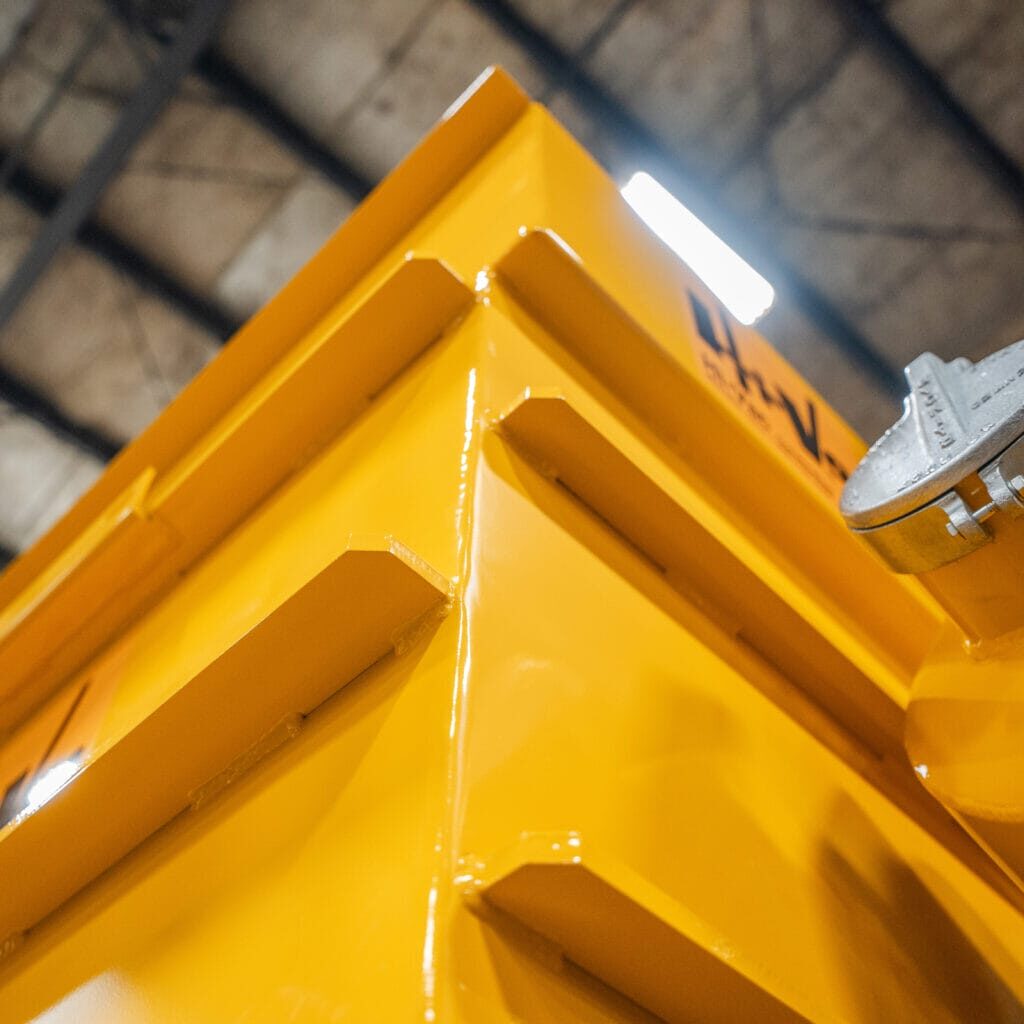 Bright yellow welded metal corner with reinforced ribs and a round filler cap on a Hi‑Vac industrial vacuum tank