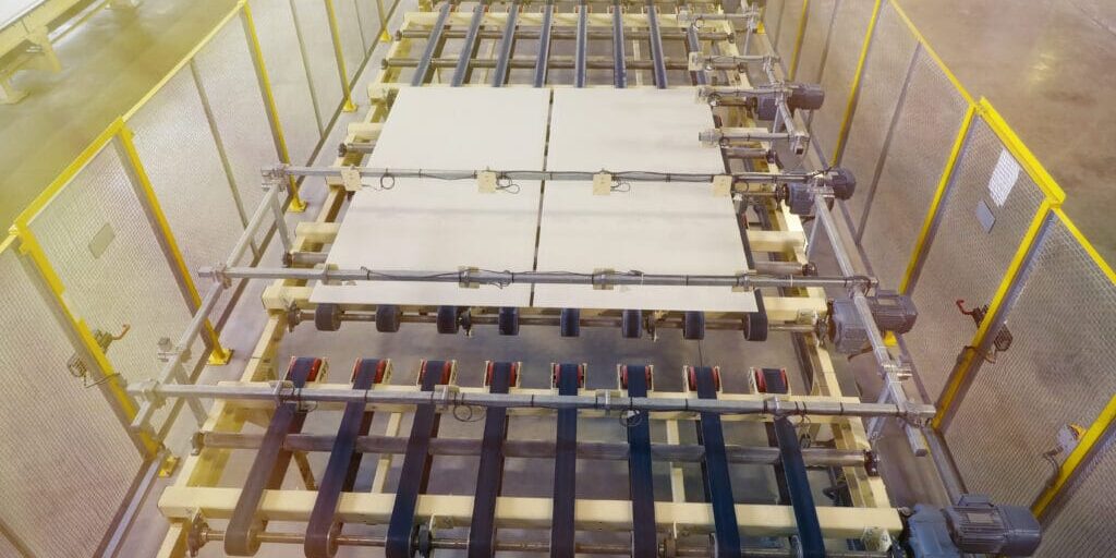 Overhead view of roller-and-belt conveyor moving flat panels inside Hi‑Vac Industrial plant, yellow safety fencing