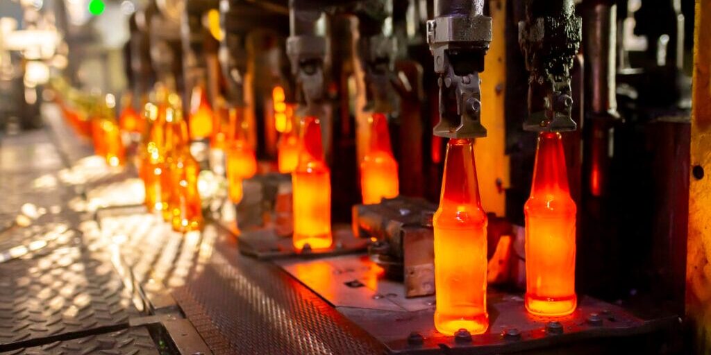 Glowing glass bottles on an automated production line under mechanical molds, part of industrial manufacturing.